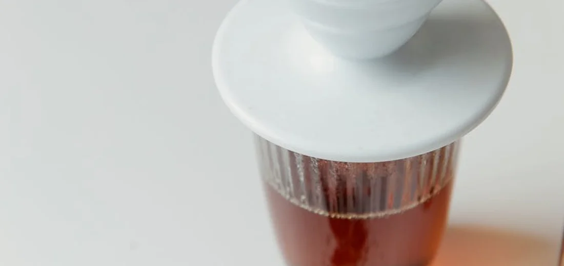 Close-up of a white coffee dripper perched above a glass carafe with brewed coffee