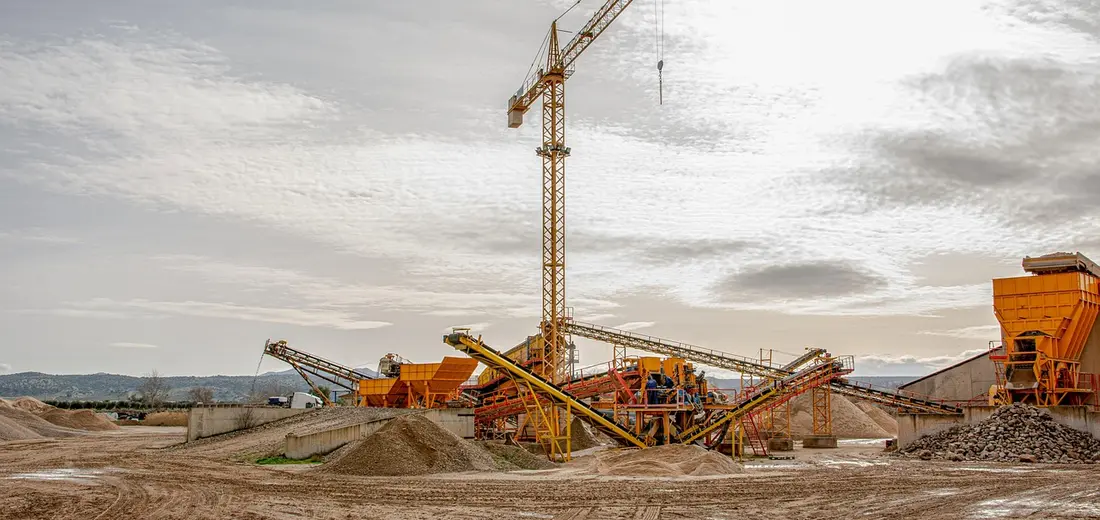 Construction site with piled gravel, a crane, and heavy machinery at work.