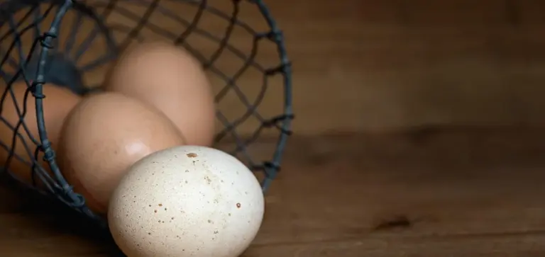 Eggs in a small black wire basket resting on a wooden surface
