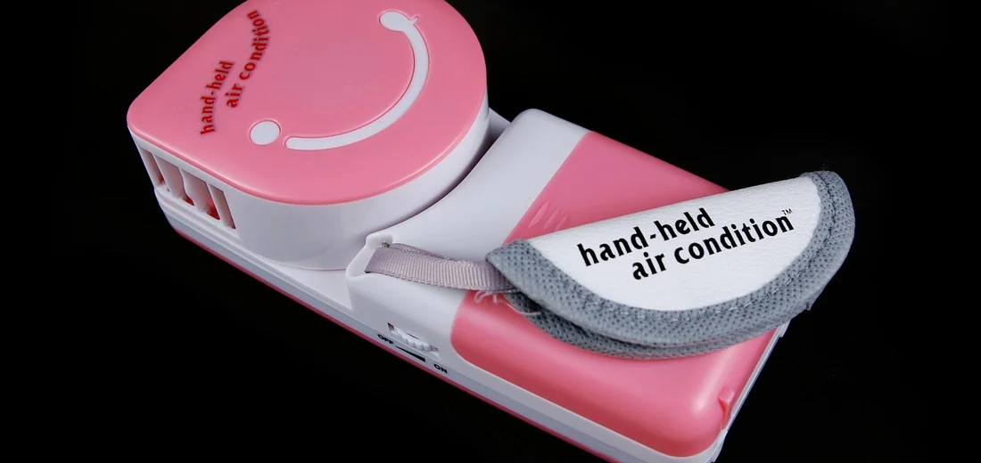 Pink and white handheld air conditioning device with a gray strap, shown against a black background.