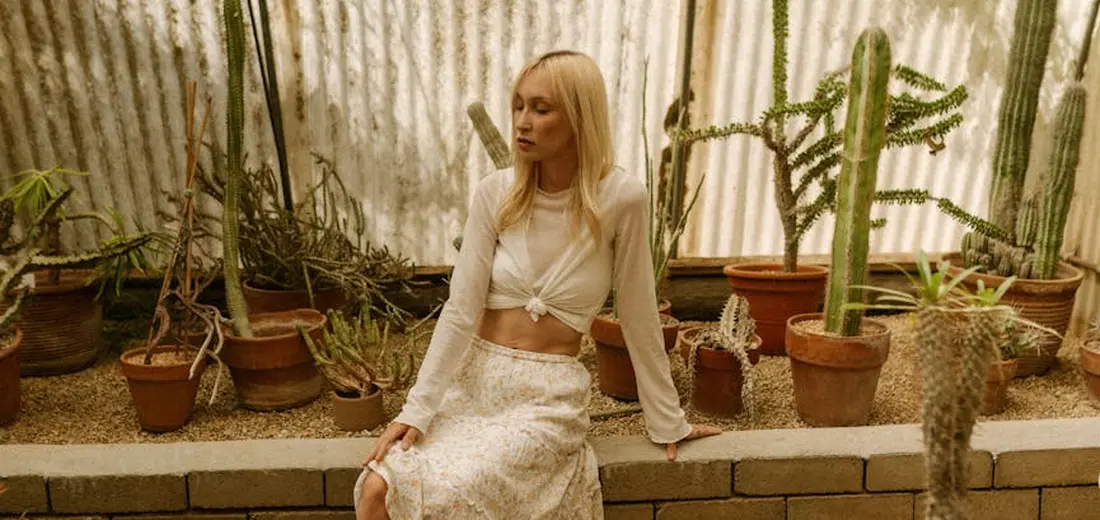 A person sits among a variety of potted succulents and cacti in a sunlit greenhouse.