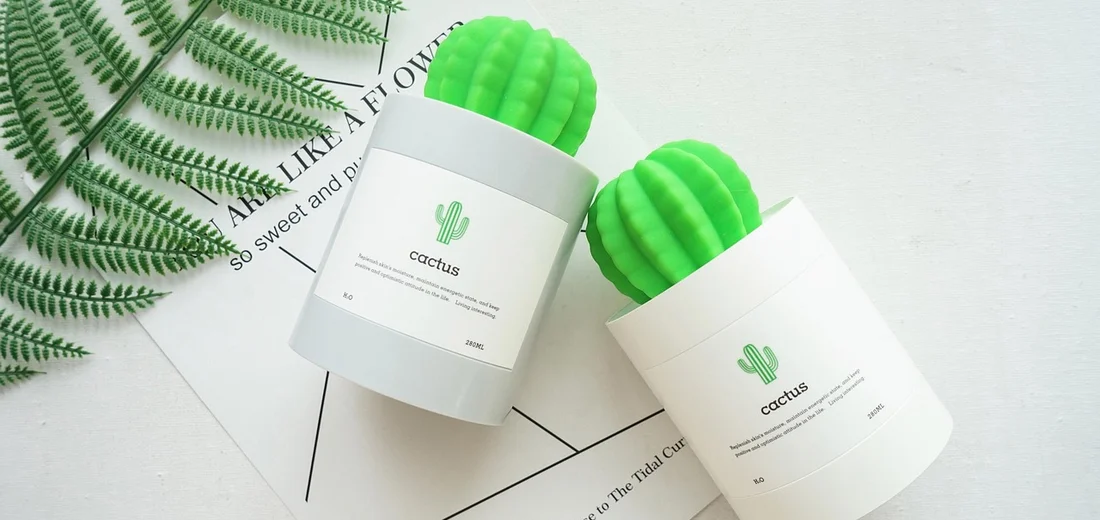 Two white pots with bright green cactus-shaped devices sitting on a white surface, with fern leaves in the background.