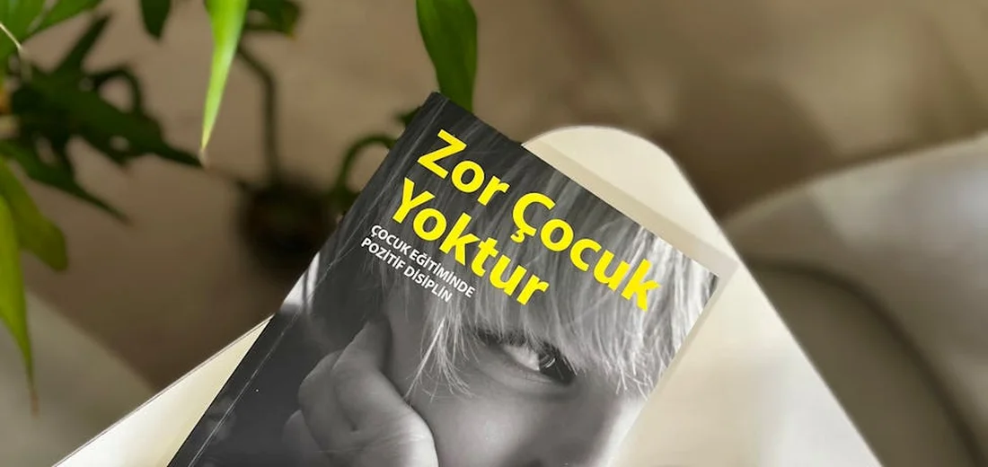 Close-up of a black-and-white magazine page with a person's face, resting on a white surface, with green plant leaves in the background.