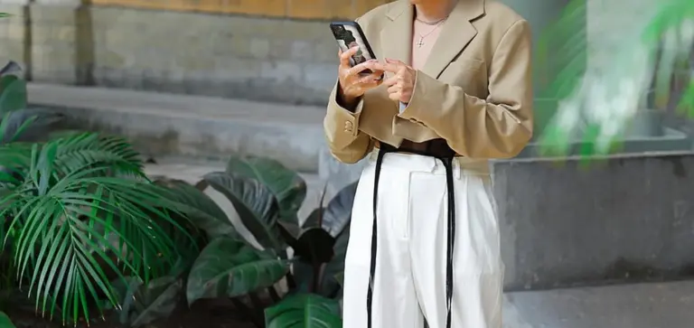 Person in a light blazer standing beside large indoor palm plants