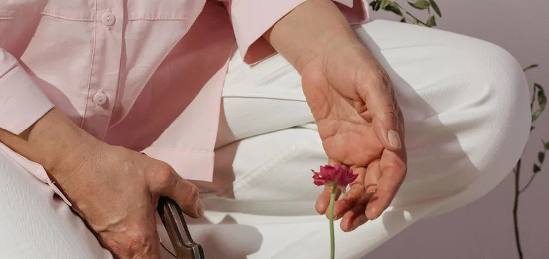 Person in a pink shirt using pruning shears to trim a small pink flower indoors.