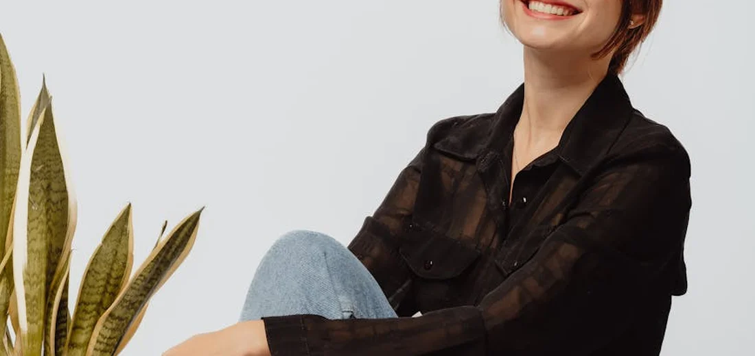 Person sitting indoors beside a snake plant, illustrating routine maintenance for a houseplant