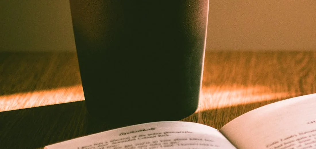Close-up of a dark plant pot on a wooden surface with an open book in the background