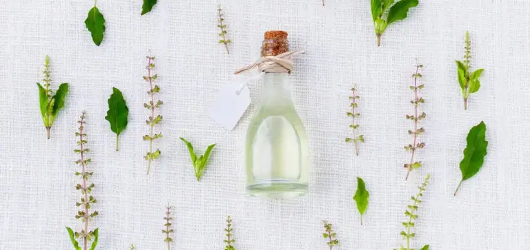 Small glass bottle with cork and tag surrounded by fresh herbs on a white textured background, representing natural, organic pest-control options.