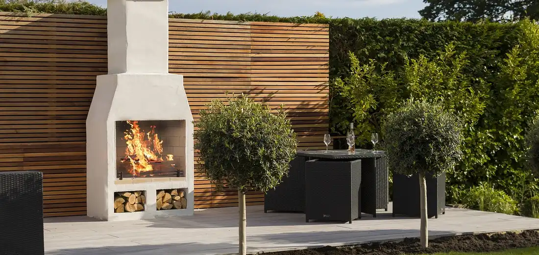 Backyard patio with a stone fireplace, wooden privacy screen, and small potted trees; a backdrop for discussing how pumice improves drainage in succulent soil mixes.