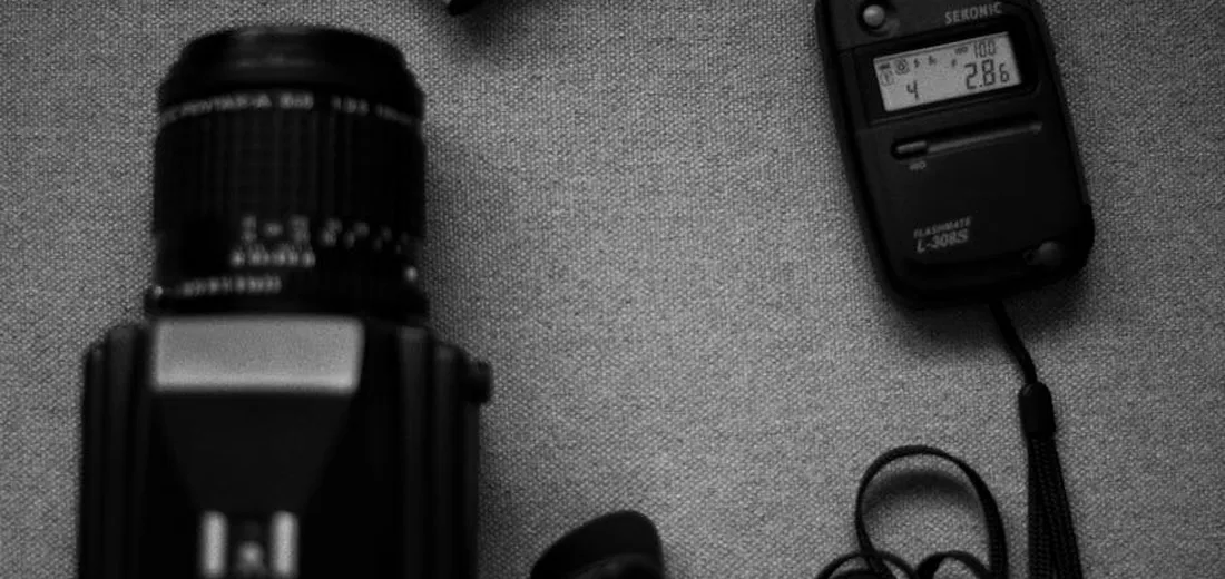 Close-up of a camera lens and a handheld light meter on a textured surface, illustrating light measurement for plants