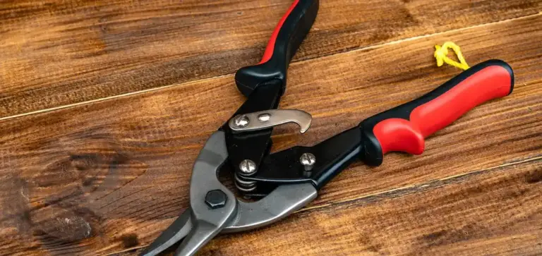 Bypass pruning shears with red and black handles resting on a wooden surface.
