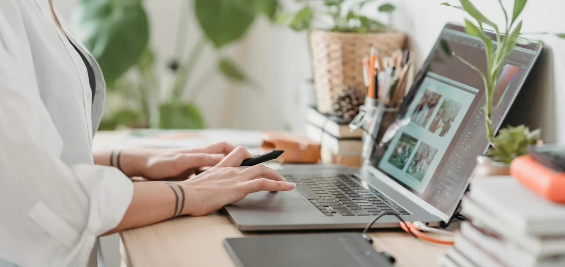 A person sits at a desk with a laptop, surrounded by potted plants, illustrating monitoring and diagnosing seasonal stress in a mixed indoor plant collection.