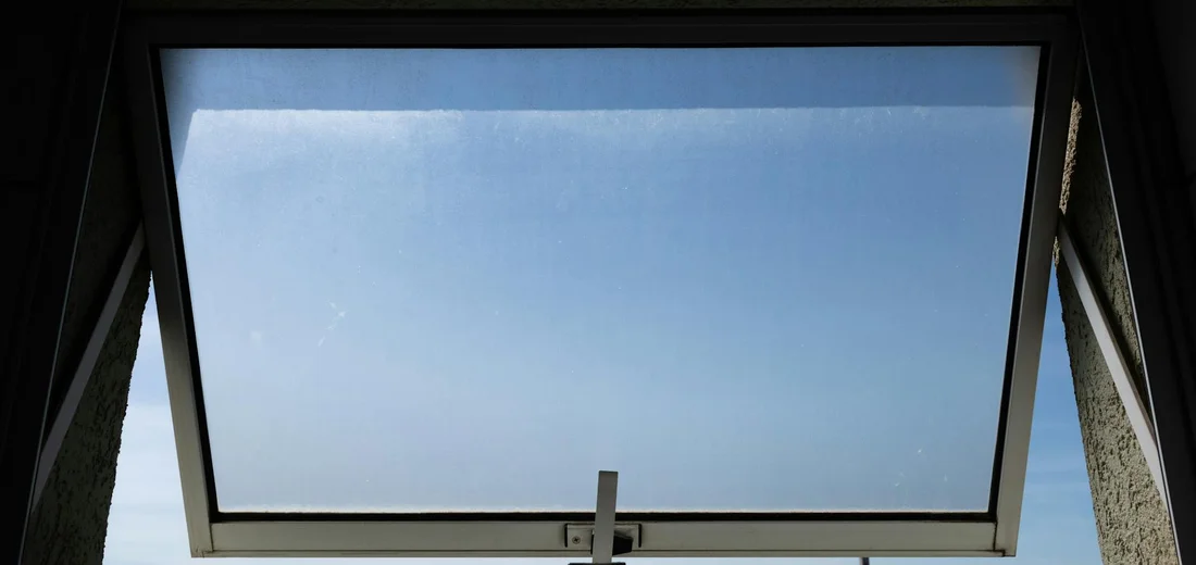Open skylight with clear blue sky, illustrating natural air exchange in an indoor space.