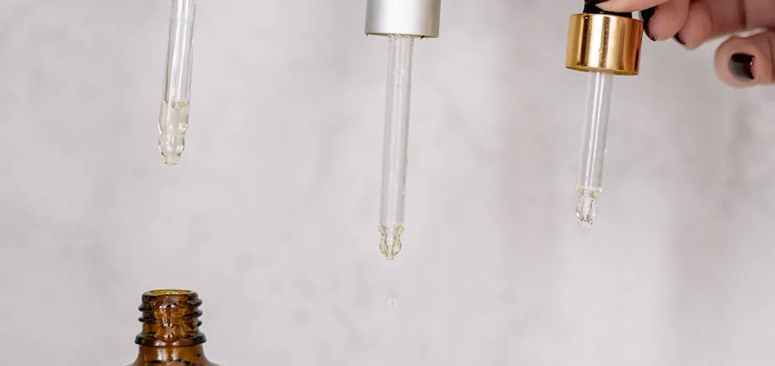 Close-up of glass droppers releasing liquid over a brown glass bottle in a clean laboratory-like setting.