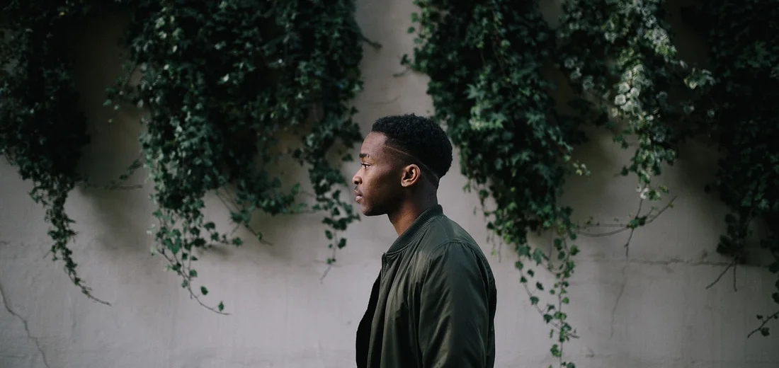 Side-profile of an individual standing in front of a wall with trailing String of Hearts vines.