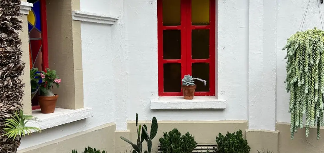 White house porch with a red window frame; small potted succulents on the windowsill and a hanging plant on the right, illustrating a gentle outdoor transition