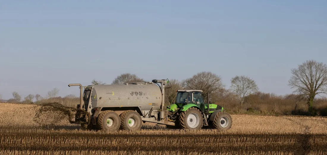 Green tractor towing a large fertilizer tank across a harvested field